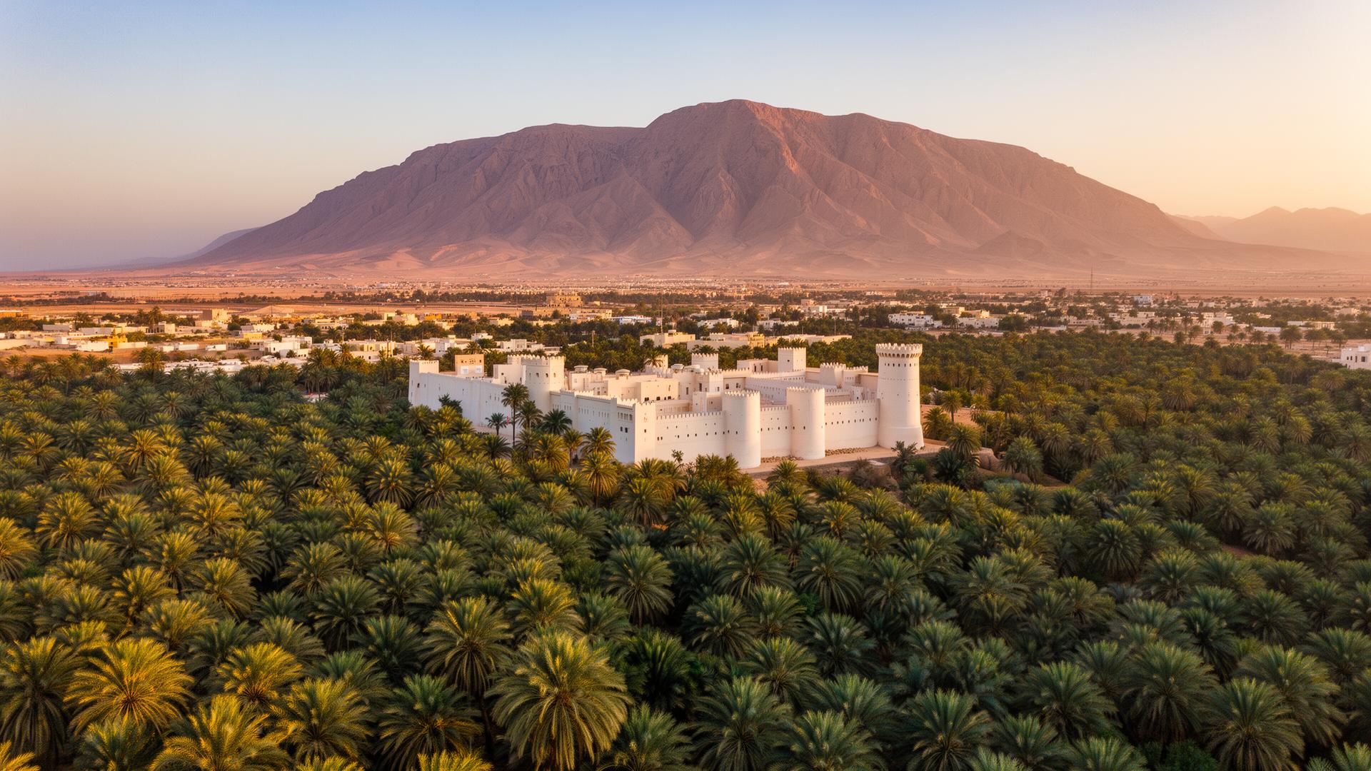 Panoramic aerial morning view of Al Ain at golden hour with the vast green Al Ain Oasis date palm groves in the foreground, the historic Al Jahili Fort with its round crenellated tower in the middle, and the dramatic Jebel Hafeet mountain rising in the distance