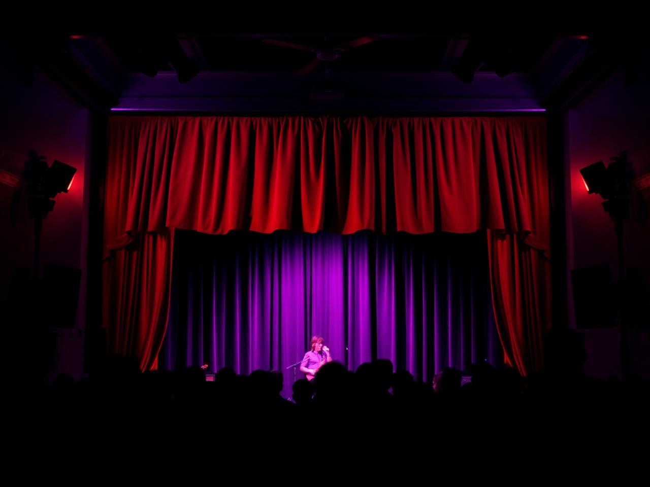 Intimate independent music and cabaret venue interior with red velvet curtains and warm purple stage lighting