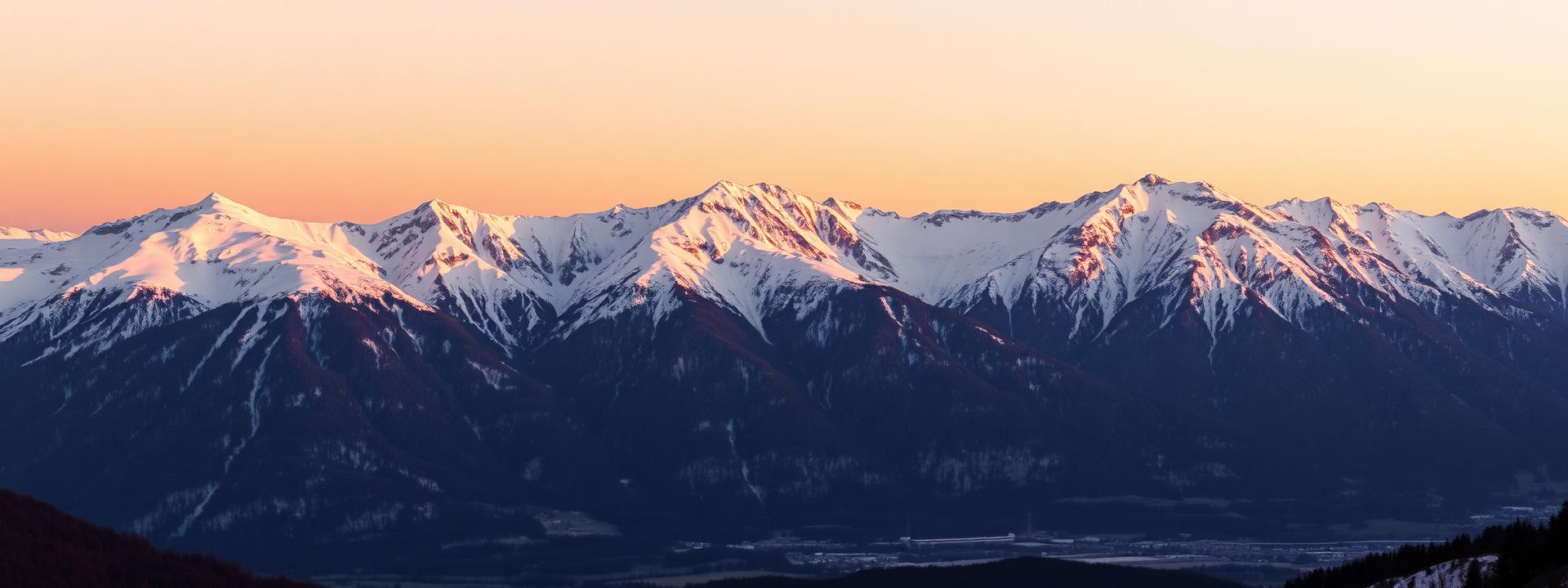 The Nordkette alpine mountains above Innsbruck at last golden light with snow-capped peaks reflecting soft pink and gold sky and the Inn valley faint below