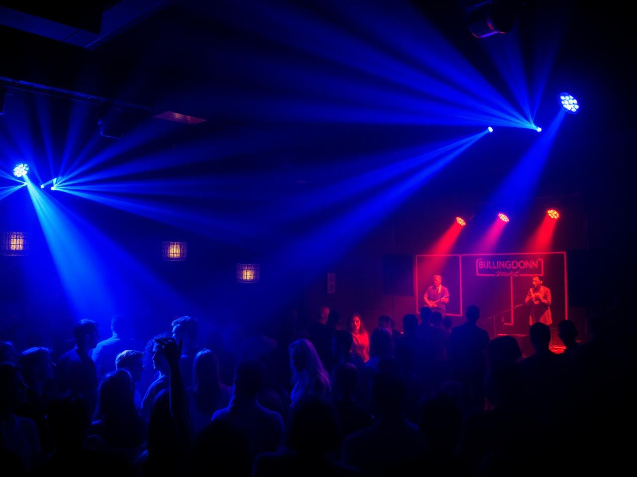 The Bullingdon nightclub Oxford interior with dramatic blue and red stage lighting, silhouetted crowd dancing in front of a small stage