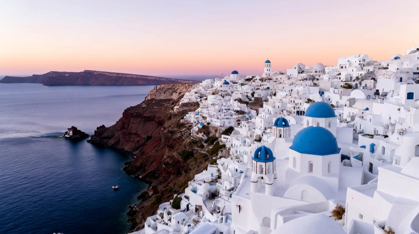 Santorini panoramic view at first light over the caldera with whitewashed Cycladic buildings cascading down the cliff of Oia, blue domed churches and the deep blue Aegean Sea below in a soft pastel sunrise sky