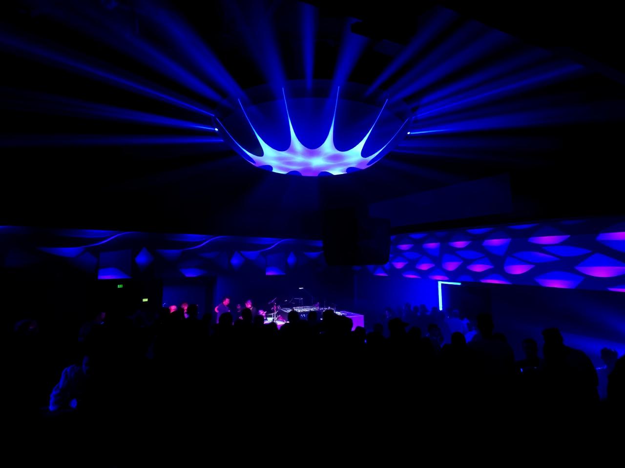 Hive Club Zurich modern techno nightclub interior with dramatic blue and purple LED lighting, raised DJ booth and a silhouetted crowd dancing